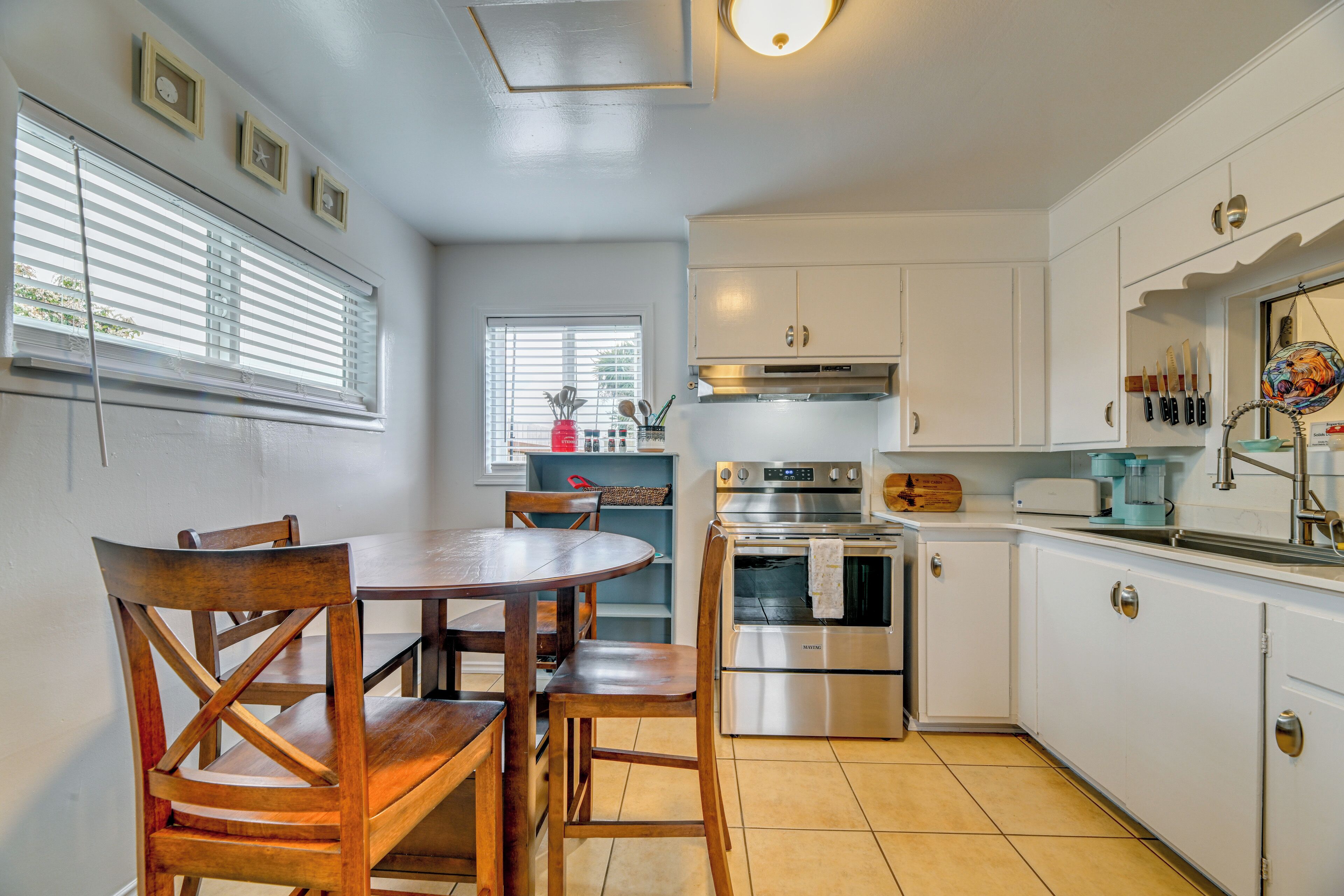A kitchen with white cabinets, a stainless steel oven, and a dining table with wooden chairs.