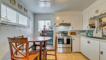 A kitchen with white cabinets, a stainless steel oven, and a dining table with wooden chairs.