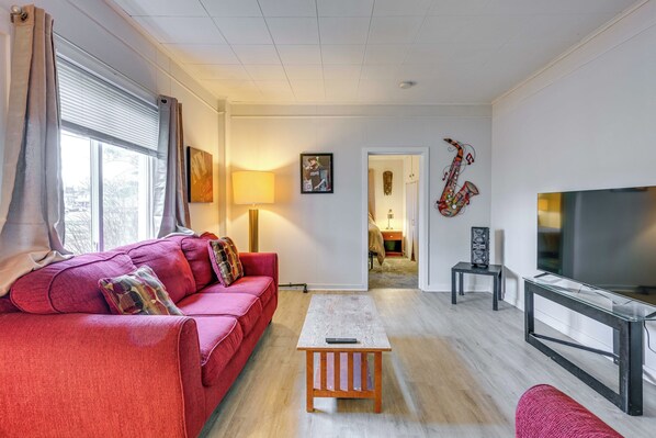 Un salon avec un canapé rouge, une table basse, un téléviseur et un saxophone servant de décoration.
