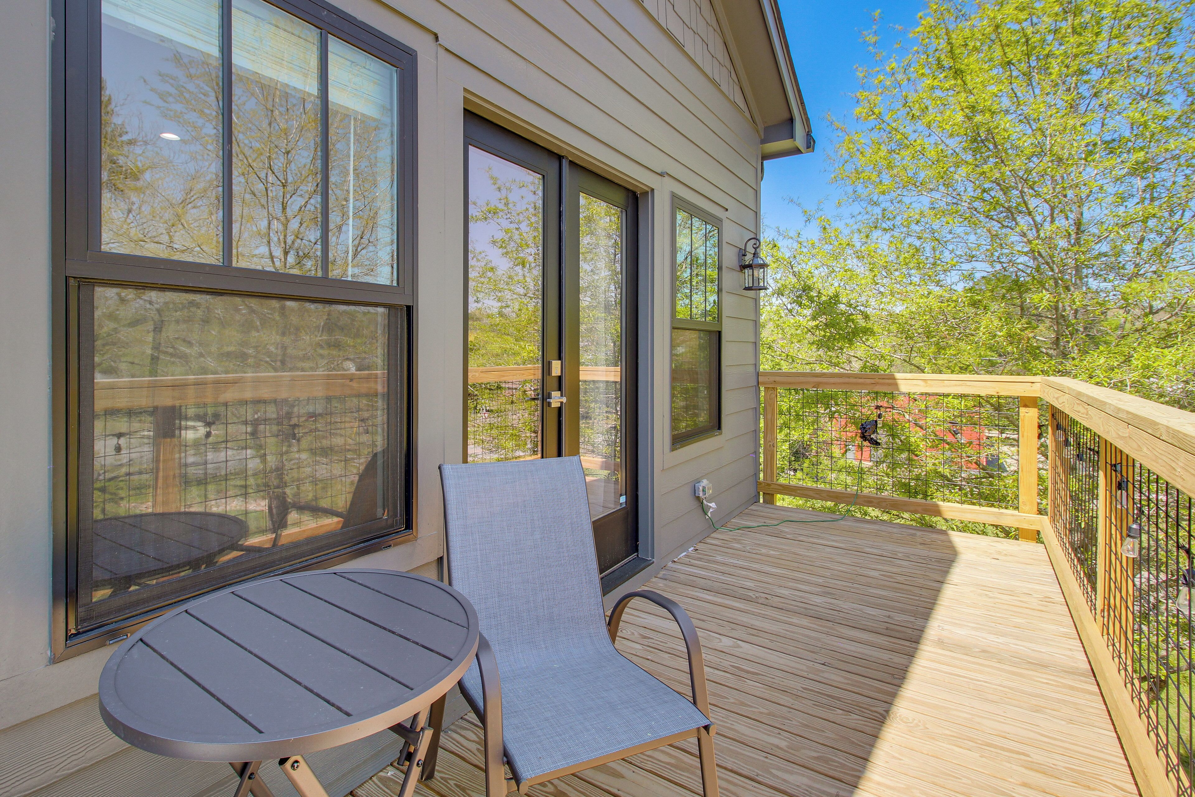 A deck with a table and chair, large windows, and a view of trees and a fence.