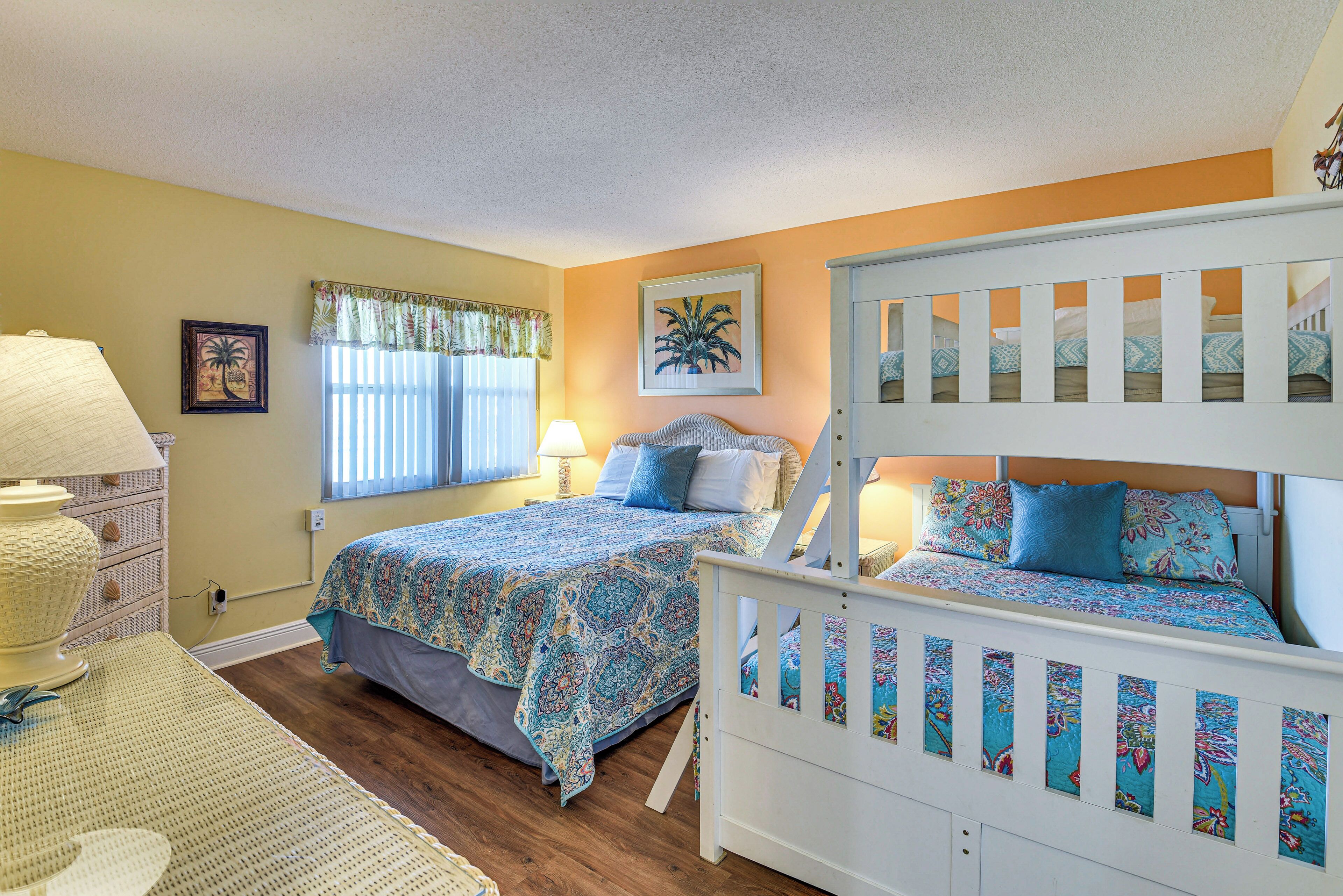 A bedroom with two beds, a window with curtains, a wall-mounted lamp, and a framed picture.