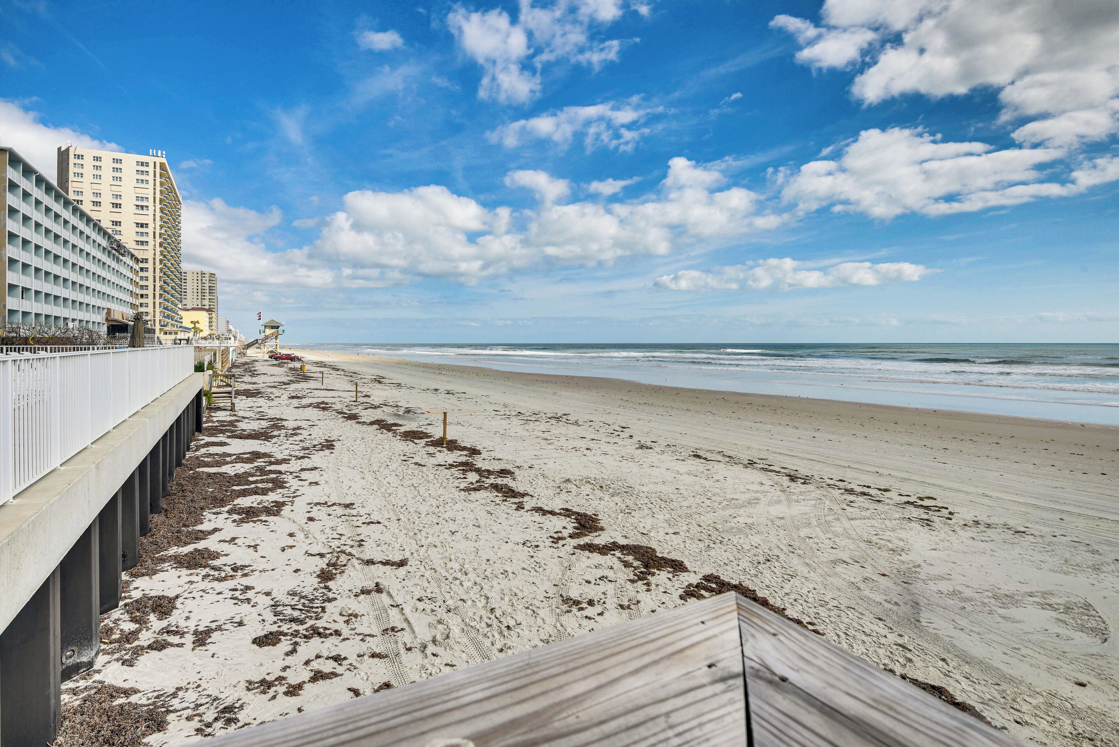 A beach with a wooden walkway, a hotel with a unique architecture, and the ocean in the background.