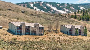 Un bâtiment moderne doté de nombreux balcons, situé sur une colline, avec en arrière-plan des arbres et un ciel dégagé.