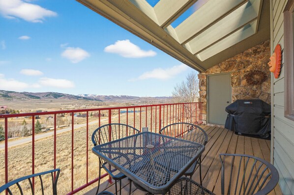 A covered outdoor area with a table and chairs, a barbecue grill, and a view of a mountainous landscape.