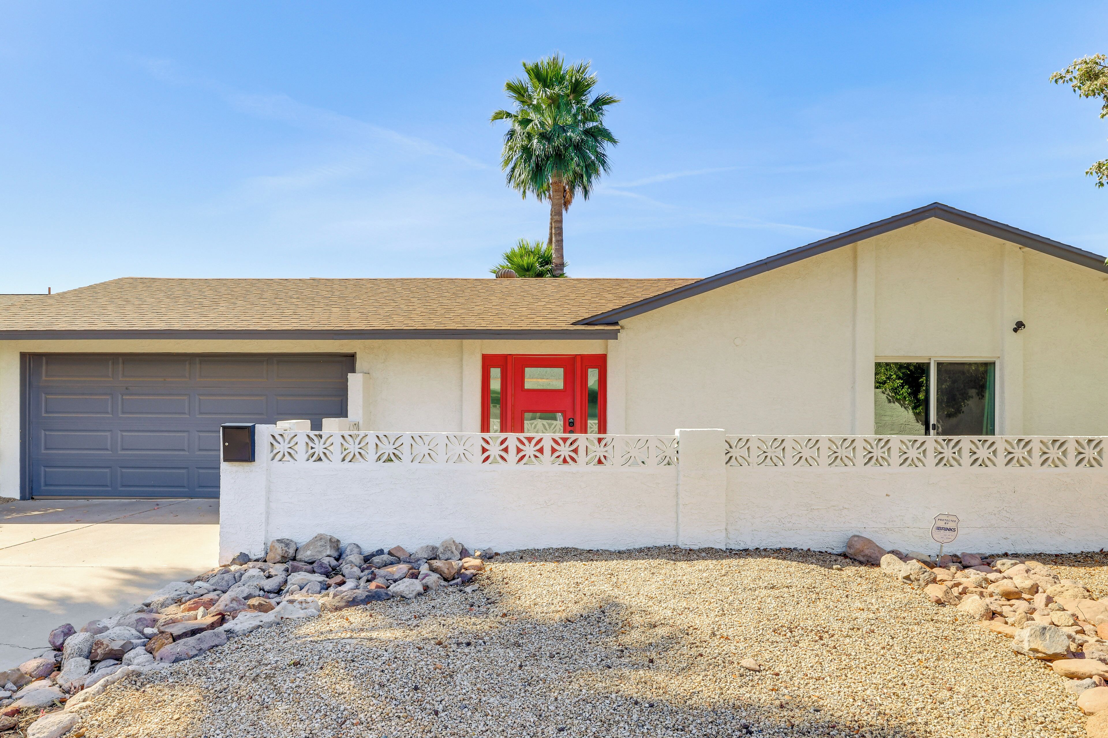 A single-story house with a red door, a garage, and a palm tree.