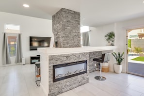 A modern living room with a stone fireplace, a flat-screen TV, and a large window.