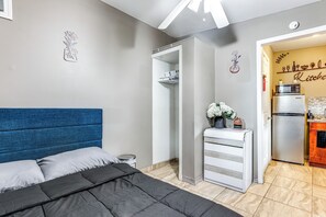 A bedroom with a bed, a wardrobe, a small table with a vase, and a kitchen area with a refrigerator and microwave. - Private Patio & Yard: East Orlando Extended Stay (Orlando)