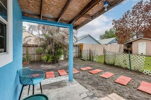 A covered patio area with a blue chair, red stepping stones, and a wooden fence. - Private Patio & Yard: East Orlando Extended Stay (Orlando)
