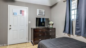 A bedroom with a bed, a dresser, a television, and a window with curtains. - Private Patio & Yard: East Orlando Extended Stay (Orlando)