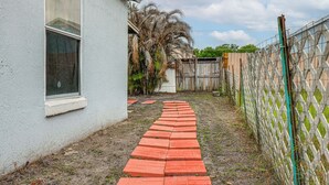 A paved pathway leading to a house with a window and a fenced yard. - Private Patio & Yard: East Orlando Extended Stay (Orlando)