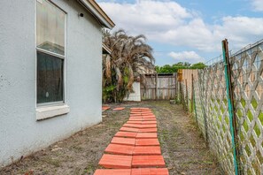 Um caminho pavimentado que leva a uma casa com janela e quintal cercado.