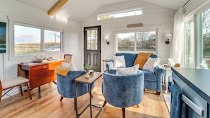 A modern interior with a wooden desk, blue armchairs, a sofa, and a dining table. - Little Blue Cabin! Country Stay Near Williamsport (Allenwood)