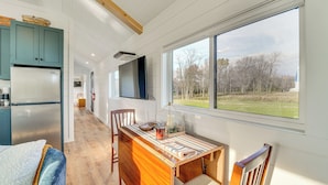 A modern kitchen with a built-in refrigerator, wooden dining table, and a large window offering a view of a grassy field. - Little Blue Cabin! Country Stay Near Williamsport (Allenwood)