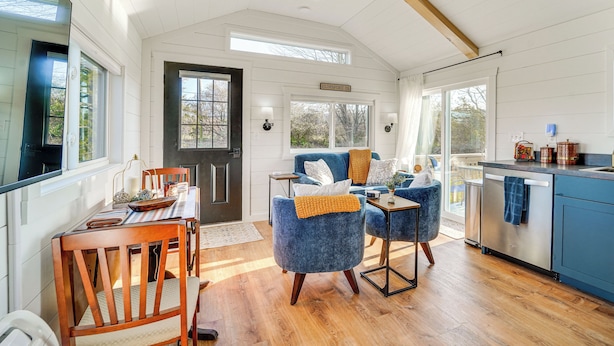 A spacious kitchen with wooden cabinetry, a dining area with a wooden table and chairs, and a cozy seating area with blue upholstered chairs. - Little Blue Cabin! Country Stay Near Williamsport (Allenwood)