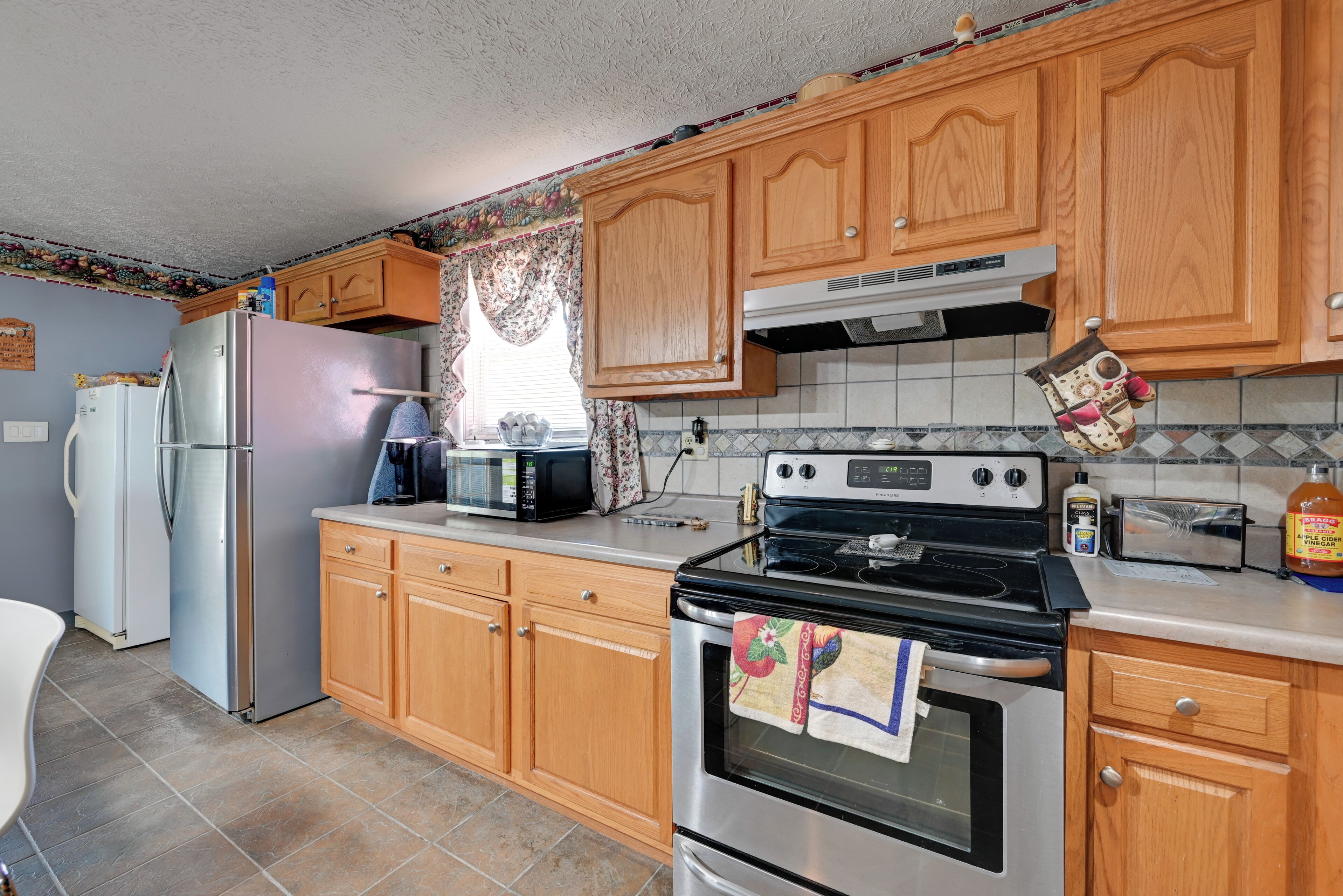 A kitchen with wooden cabinets, a stainless steel refrigerator, a microwave, a stove, and a toaster.