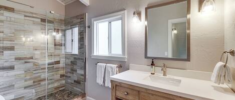 A bathroom with a glass shower enclosure, a white sink, wooden vanity, and a large mirror.