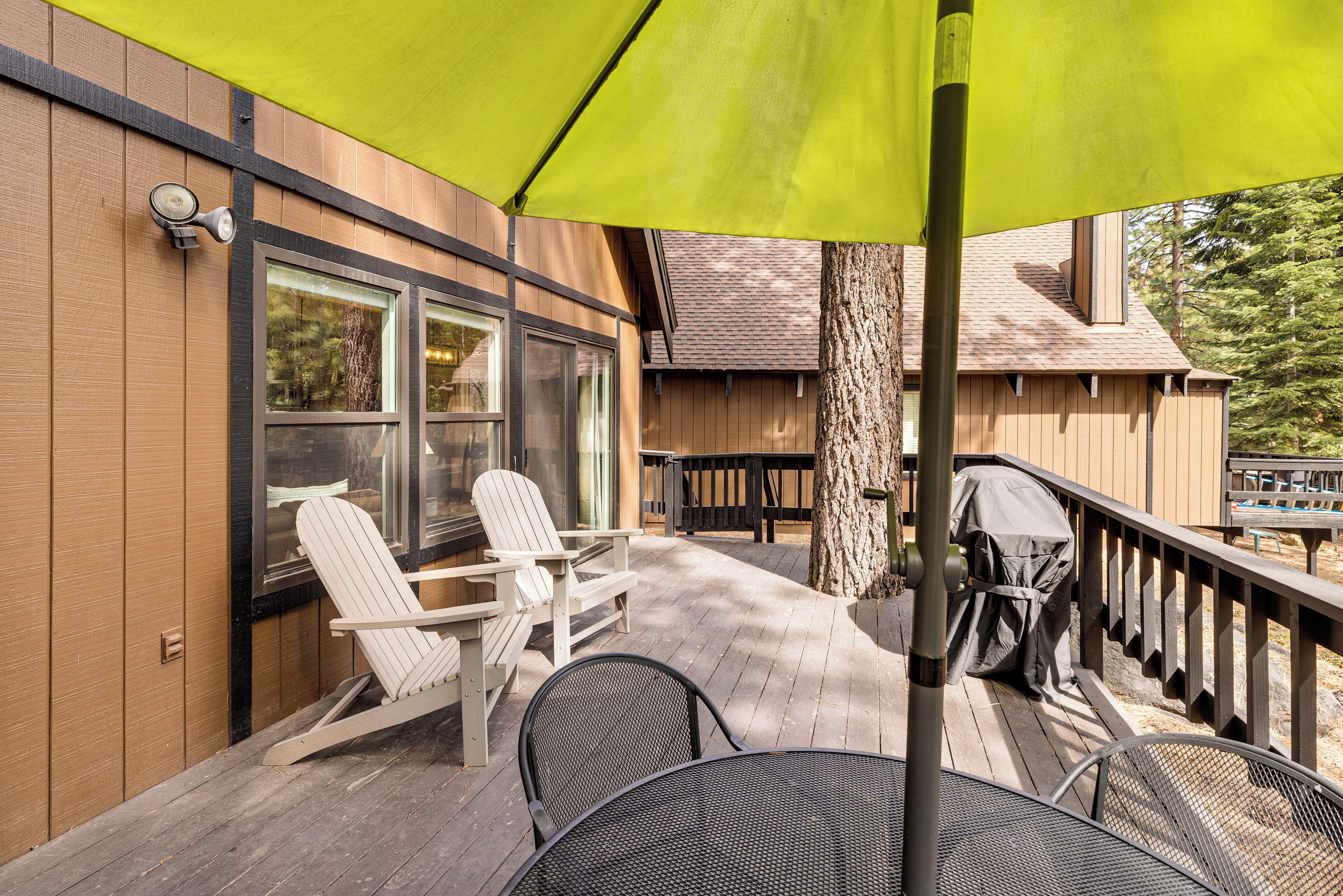 A wooden deck with outdoor seating, a covered grill, and a large umbrella.