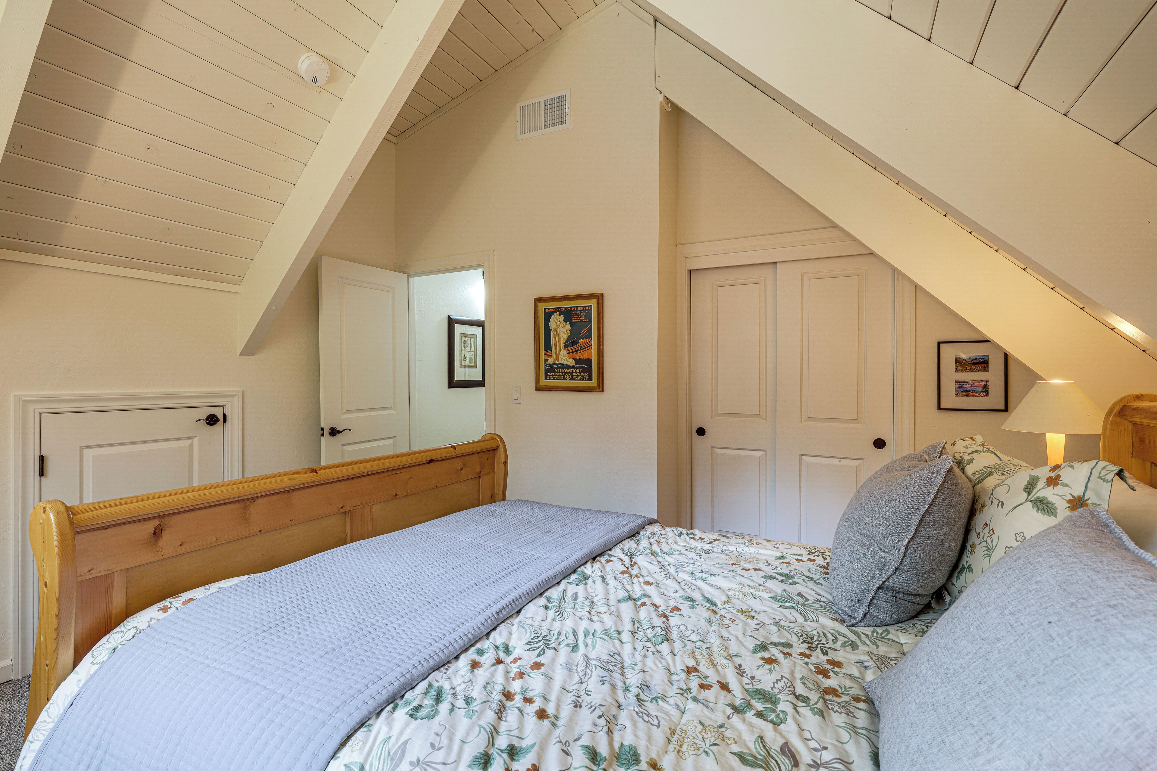 Un dormitorio con techo inclinado, estructura de cama de madera, colcha estampada y dos puertas.