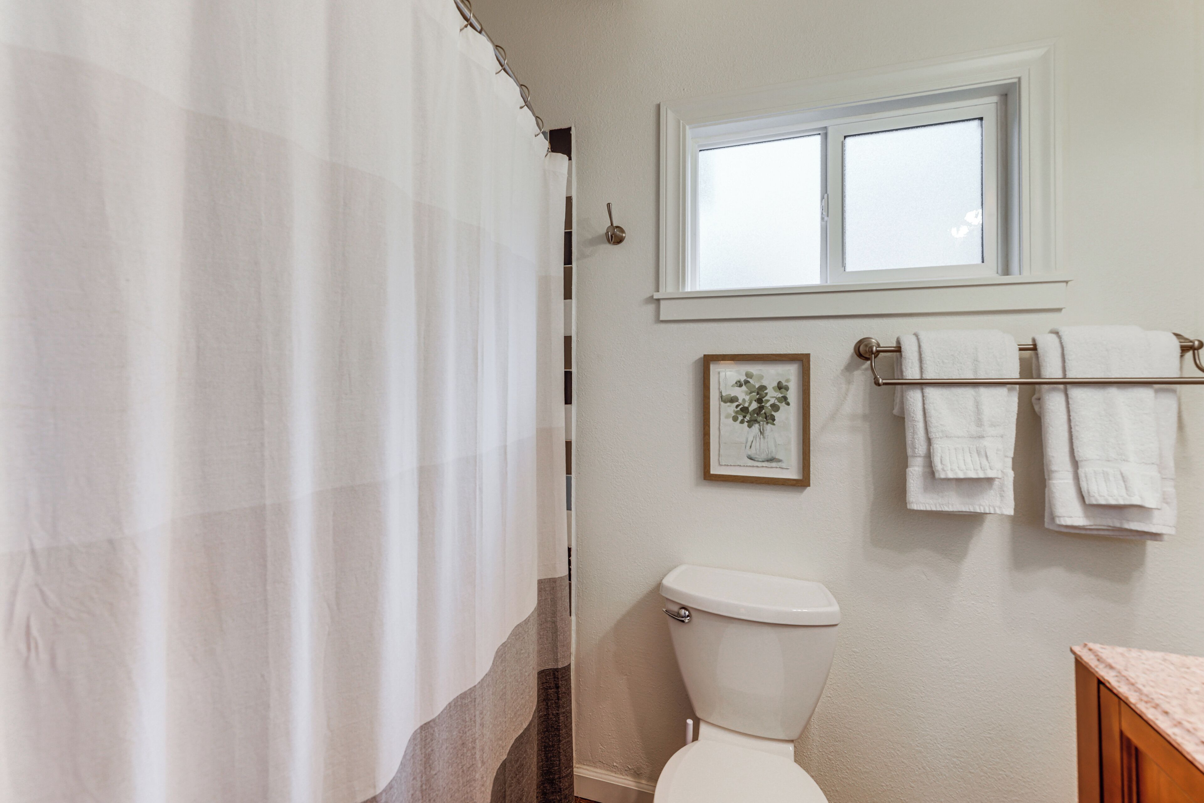 Een badkamer met toilet, een raam, een douchegordijn en een handdoekrek met handdoeken.