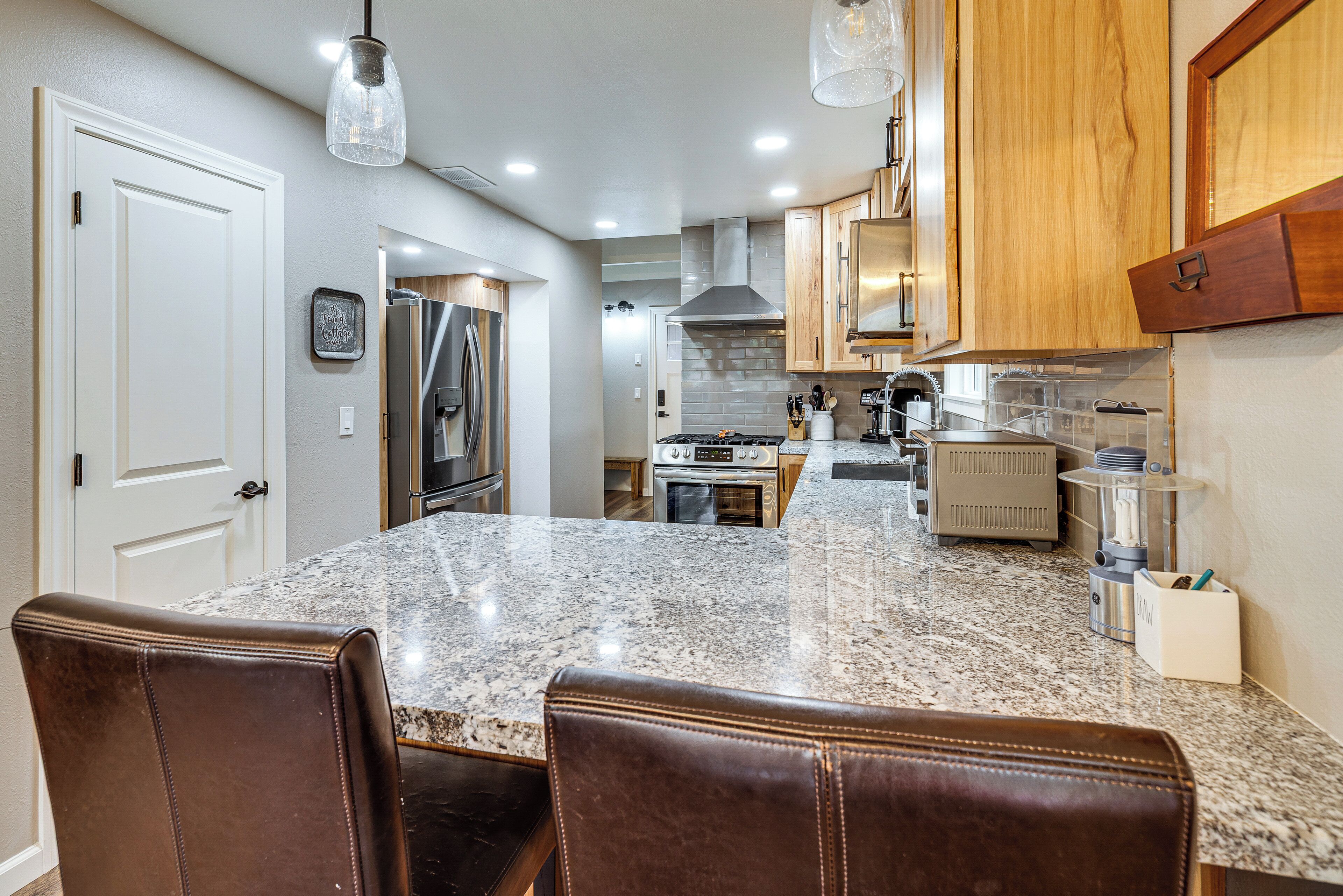 A kitchen with granite countertops, wooden cabinets, and a dining area with leather chairs.
