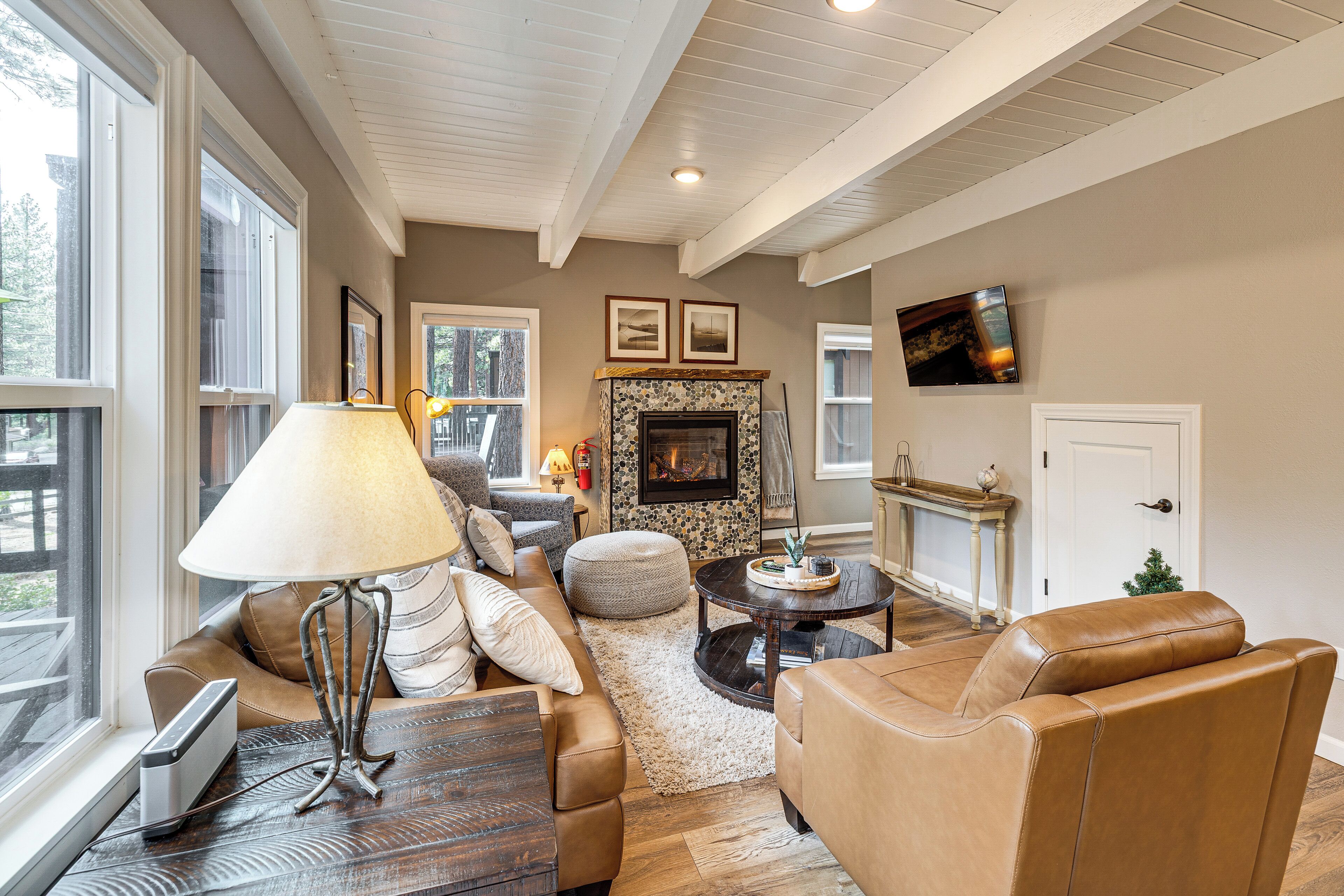 A living room with a fireplace, leather furniture, a TV, and large windows.