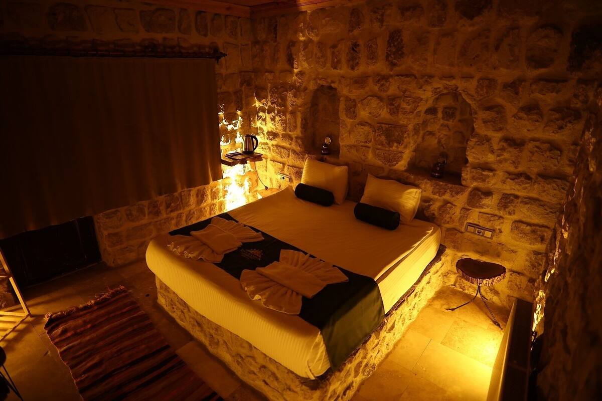 Un dormitorio de paredes de piedra con cama, almohadas, una mesita de noche y un buró.
