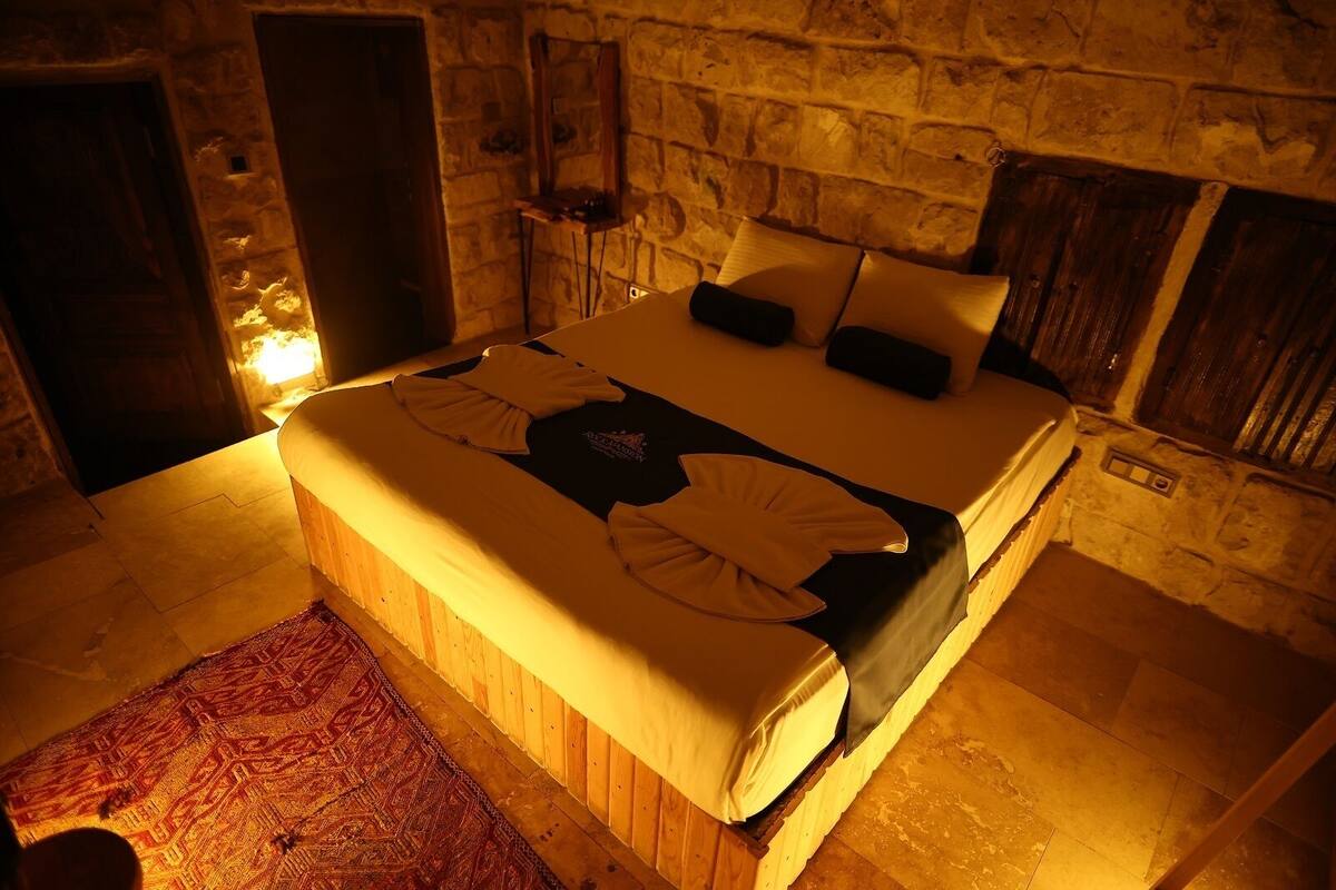 Un dormitorio con pared de piedra, cama de madera y alfombra roja estampada.