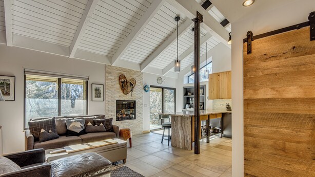 A spacious living area with a large sofa, ottoman, and a dining area with a kitchen in the background. - Walk to Town & Slopes, Views, SPA & Sauna Access (Ketchum)