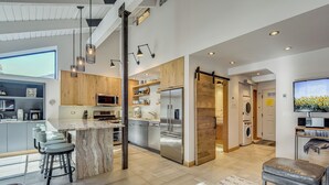 A modern kitchen with a central island, bar stools, and a dining area with a sofa and ottoman. - Walk to Town & Slopes, Views, SPA & Sauna Access (Ketchum)