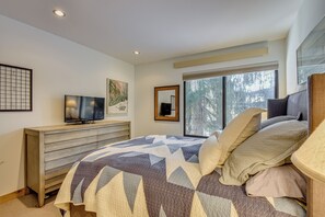 A bedroom with a bed, a TV, a dresser, a window with a view of trees, and artwork on the walls.