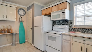 Una cocina con electrodomésticos blancos, armarios de madera, un reloj y un salpicadero con diseño de espiga.