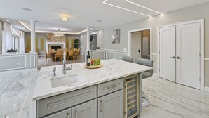 A modern kitchen with marble countertops, a built-in oven, and a dining area with a fireplace.