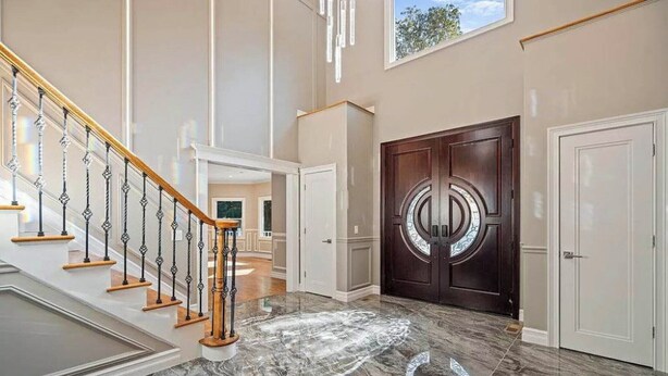 A grand staircase with a wooden handrail and black balusters, leading to a room with a large, dark wooden door with a circular design.
