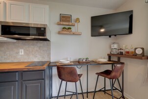Una cocina con microondas, dos taburetes de bar, una cafetera y un televisor de pantalla plana montado en la pared.