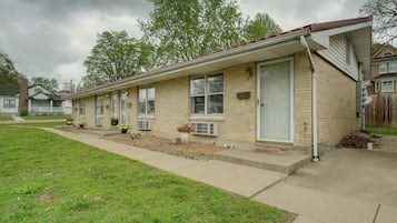 A row of single-story brick houses with attached garages, a grassy lawn, and a cloudy sky.