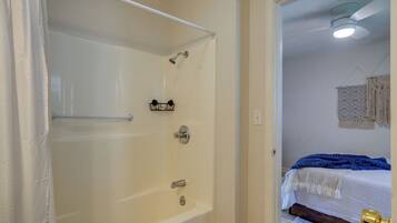 A bathroom with a bathtub, shower, and a bed with a blue blanket.