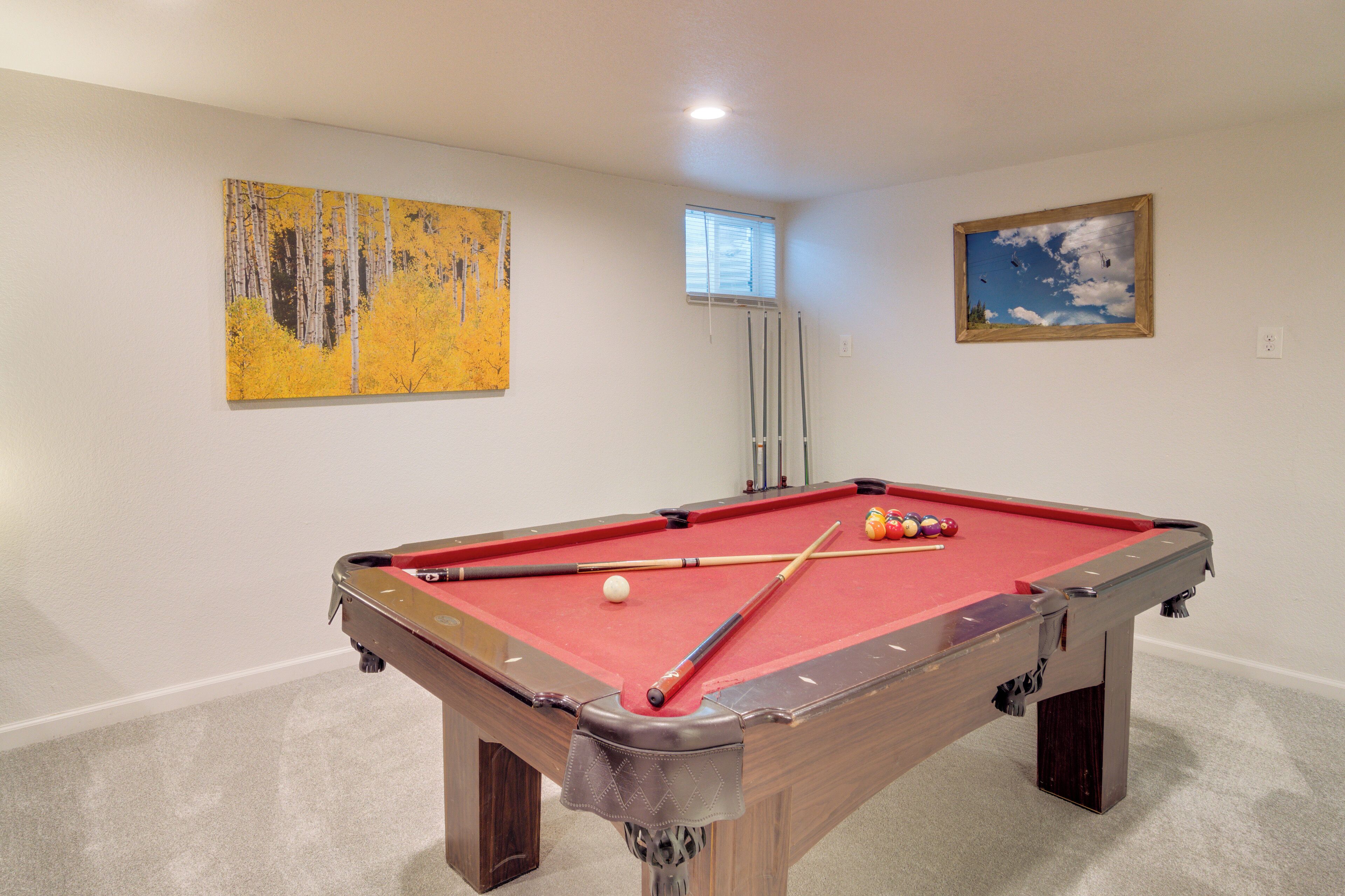 A pool table with balls, a window, and two paintings on the wall.