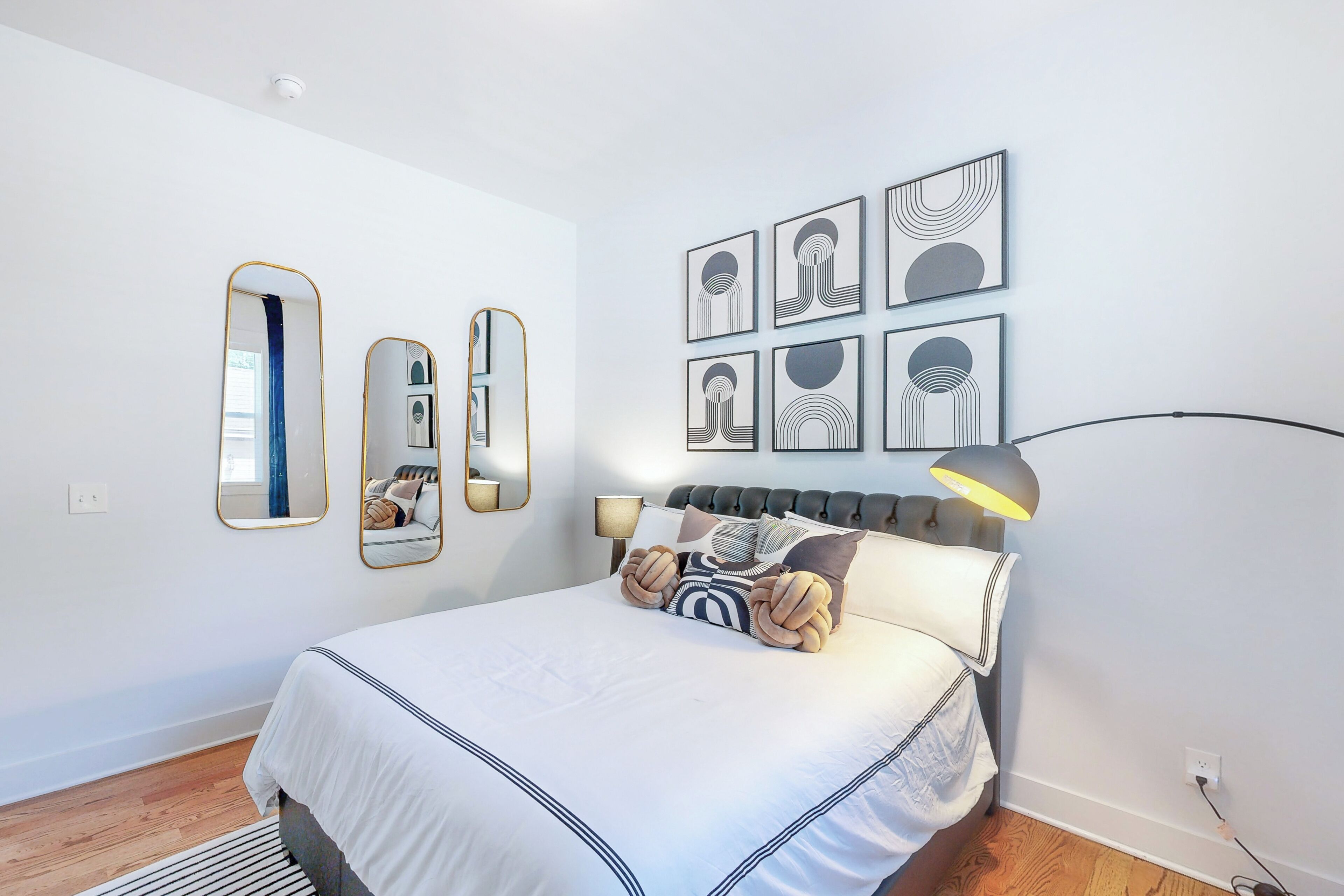 Une chambre à coucher moderne avec un grand lit, de nombreux miroirs et des œuvres d’art abstraites accrochées au mur.