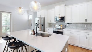 A modern kitchen with white cabinets, stainless steel appliances, and a large island with bar stools. - Atlanta Townhome: Walk to Mercedes-benz Stadium! (Atlanta)