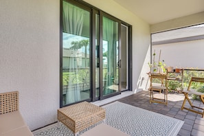 A balcony with a sliding glass door, a wicker bench, a small table, and a patterned rug. - New Home in Veranda Village w/ Resort Amenities! (Estero)