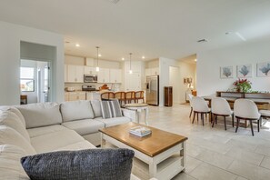 A modern living room with a sofa, coffee table, and dining area with chairs. - New Home in Veranda Village w/ Resort Amenities! (Estero)