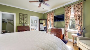 Een slaapkamer met een groot bed, een plafondventilator, een dressoir, een stoel, een bureau en een raam met gordijnen.