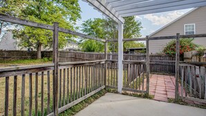 A covered patio area with a wooden fence, a concrete pathway, and a house in the background.