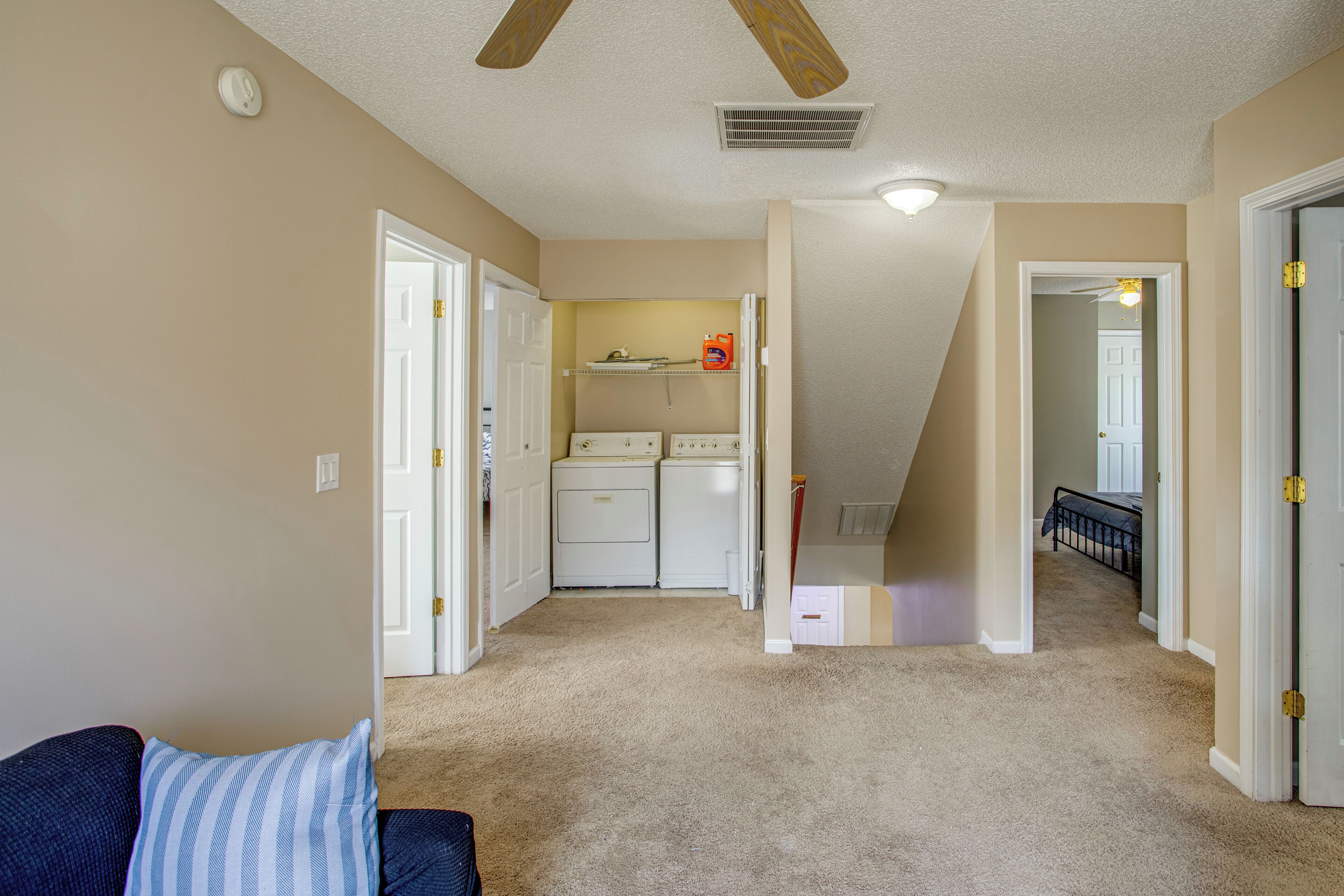 A laundry room with a washing machine and dryer, a ceiling fan, and a hallway leading to a bedroom.