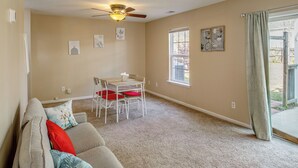 A living room with a ceiling fan, a dining table with chairs, a sofa with cushions, and a large window with curtains.