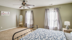 A bedroom with a bed, ceiling fan, window with curtains, and a bedside table with a lamp.