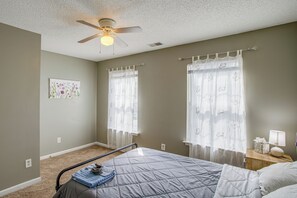 A bedroom with a bed, a ceiling fan, two windows with sheer curtains, and a bedside table with a lamp. - Great for Military Families! Quiet Columbia Home (Blythewood)
