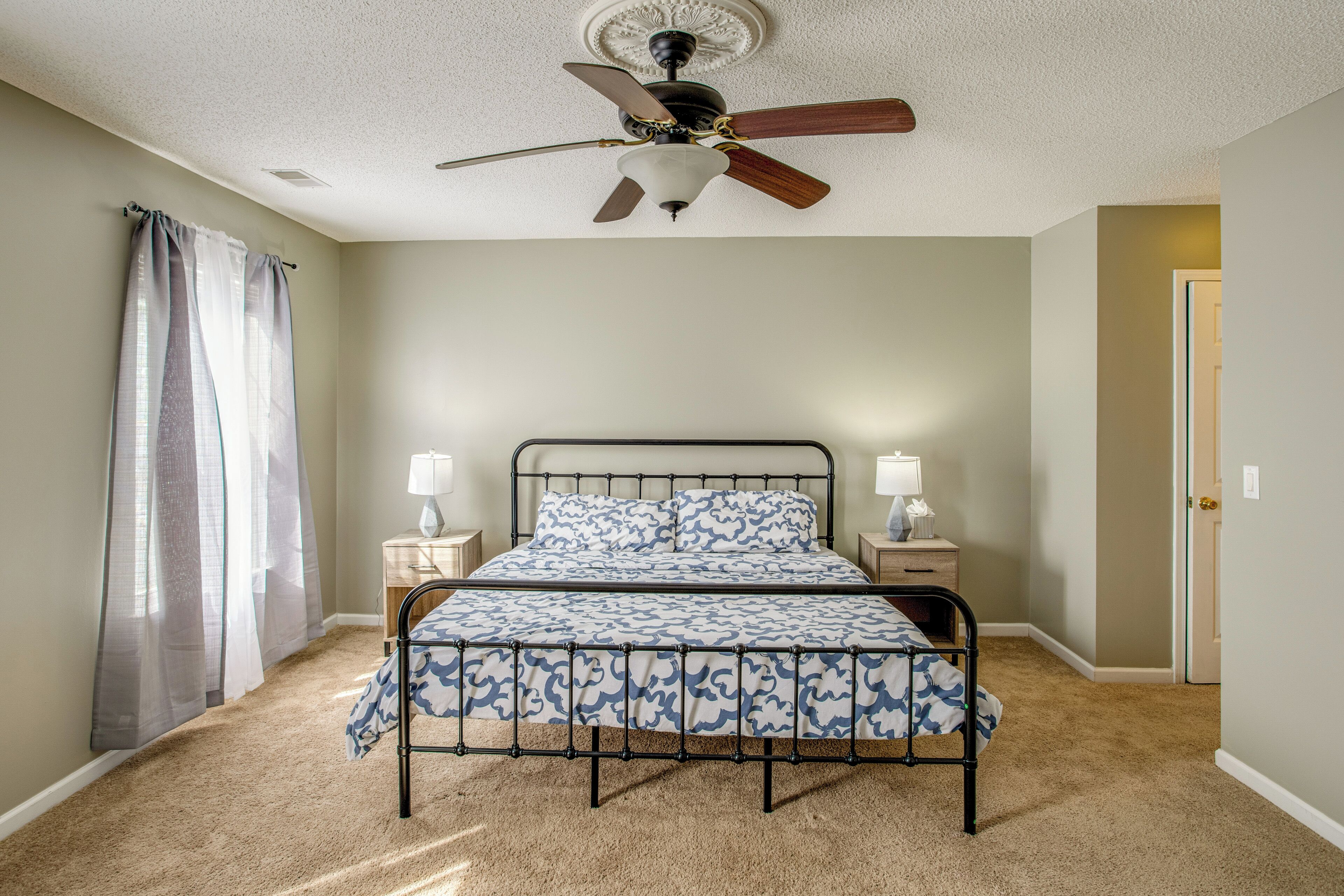 A bedroom with a bed, ceiling fan, bedside lamps, and a door.