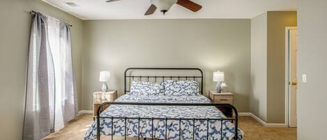 A bedroom with a bed, ceiling fan, bedside lamps, and a door.