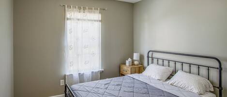A bedroom with a bed, a nightstand, a ceiling fan, and a window with a curtain.